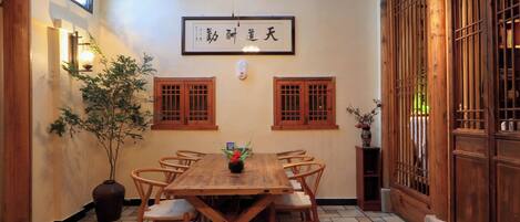 Een traditionele Japanse kamer met een houten eettafel, stoelen, een plafondventilator en een bord met Japanse tekens.