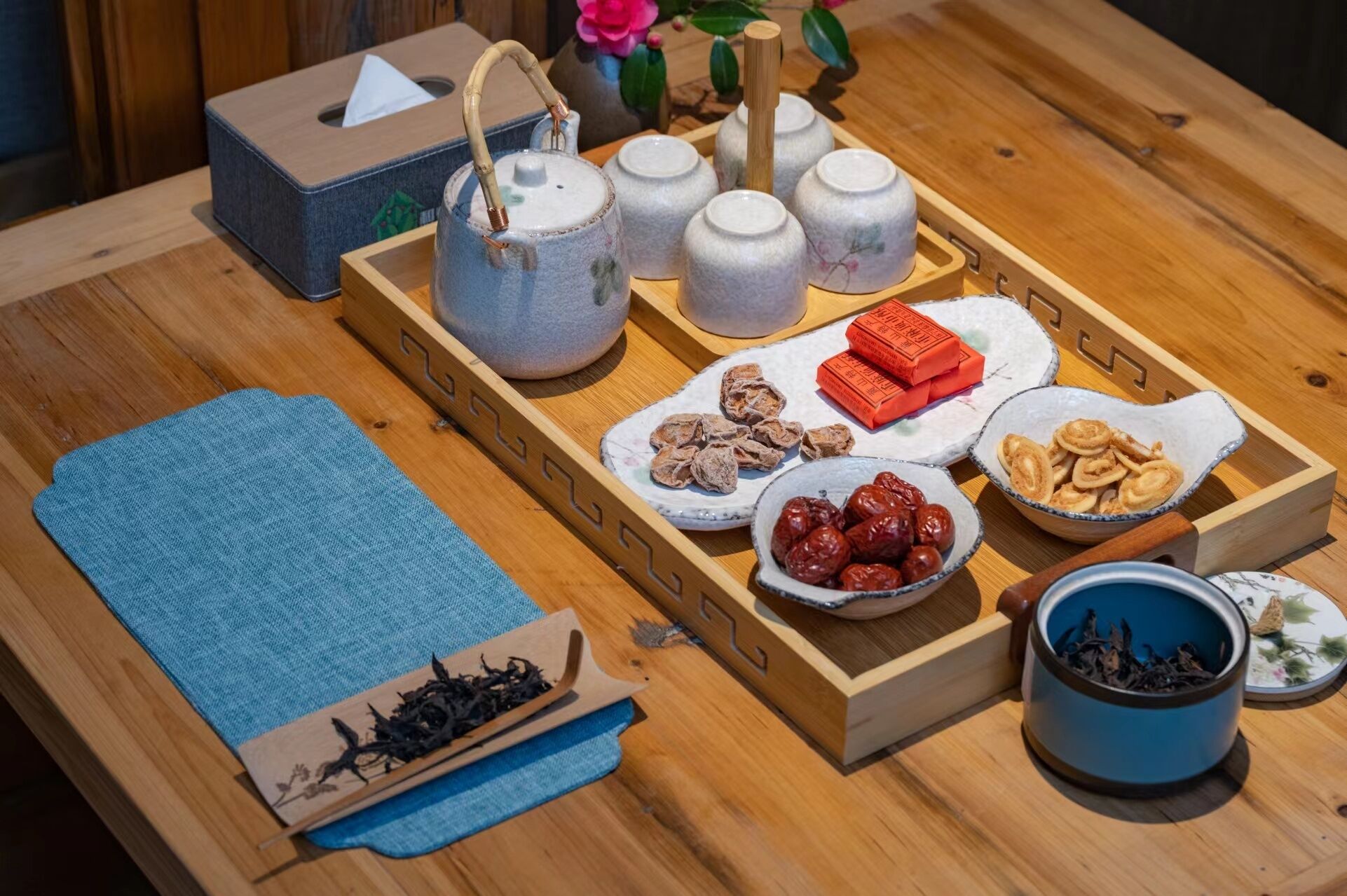 A wooden tray with tea utensils, a tissue box, and various snacks.