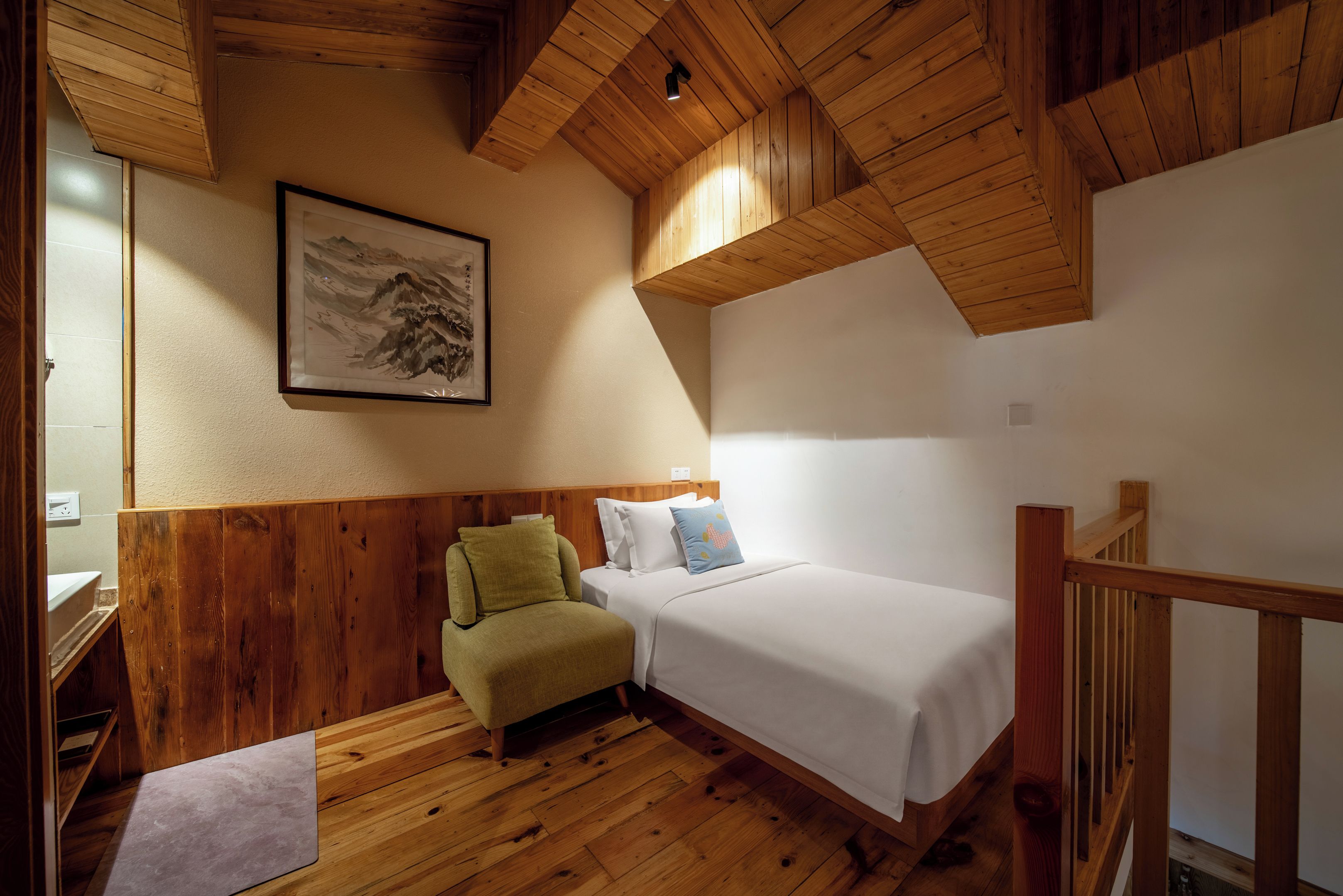 A room with wooden walls, a bed, a chair, and a painting.