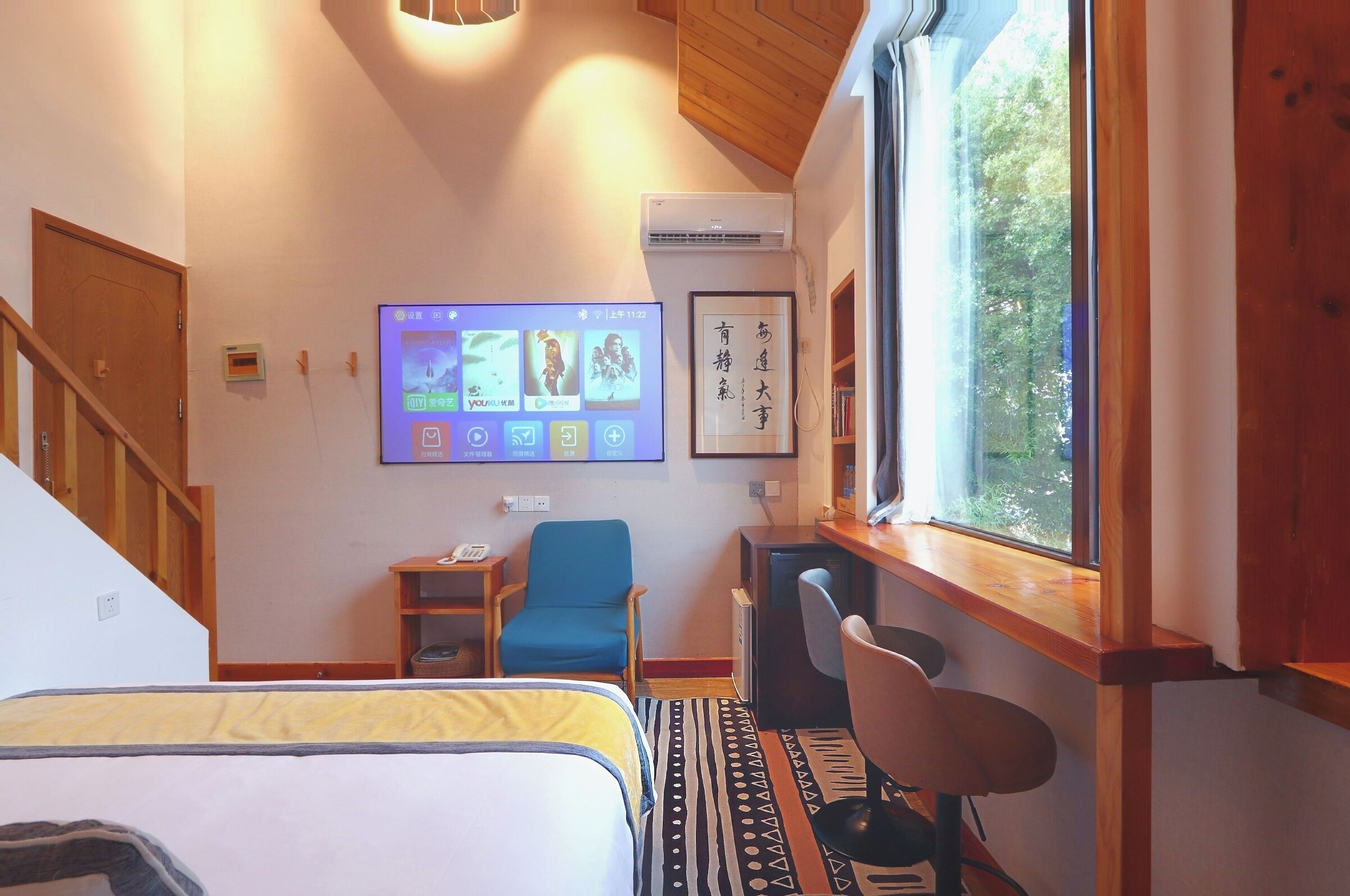 Une chambre d’hôtel avec un lit, un bureau, une chaise, un téléviseur fixé au mur et une fenêtre donnant sur un paysage verdoyant.