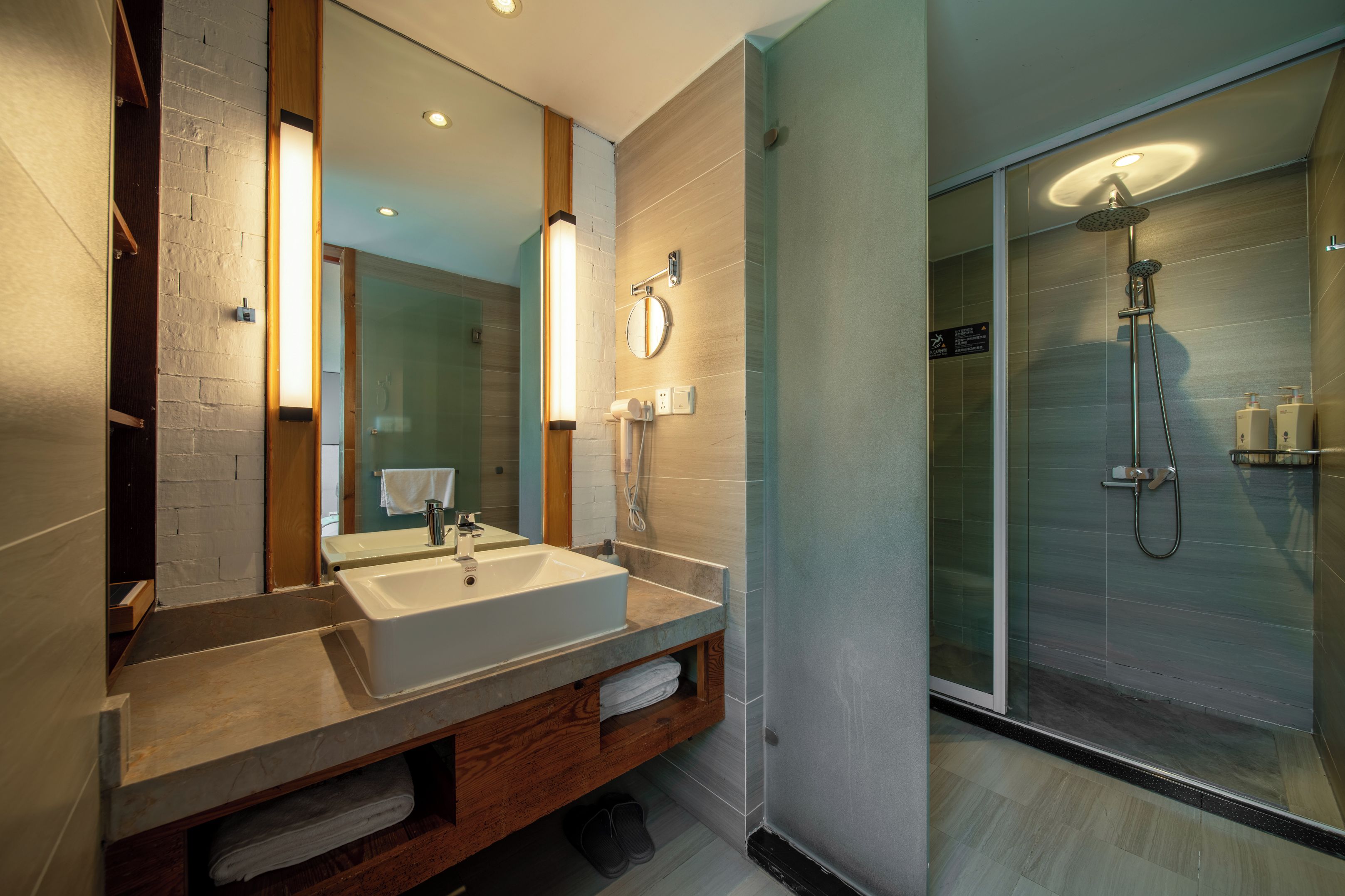 A modern bathroom with a large mirror, dual sinks, a shower with a glass door, and a wooden vanity.
