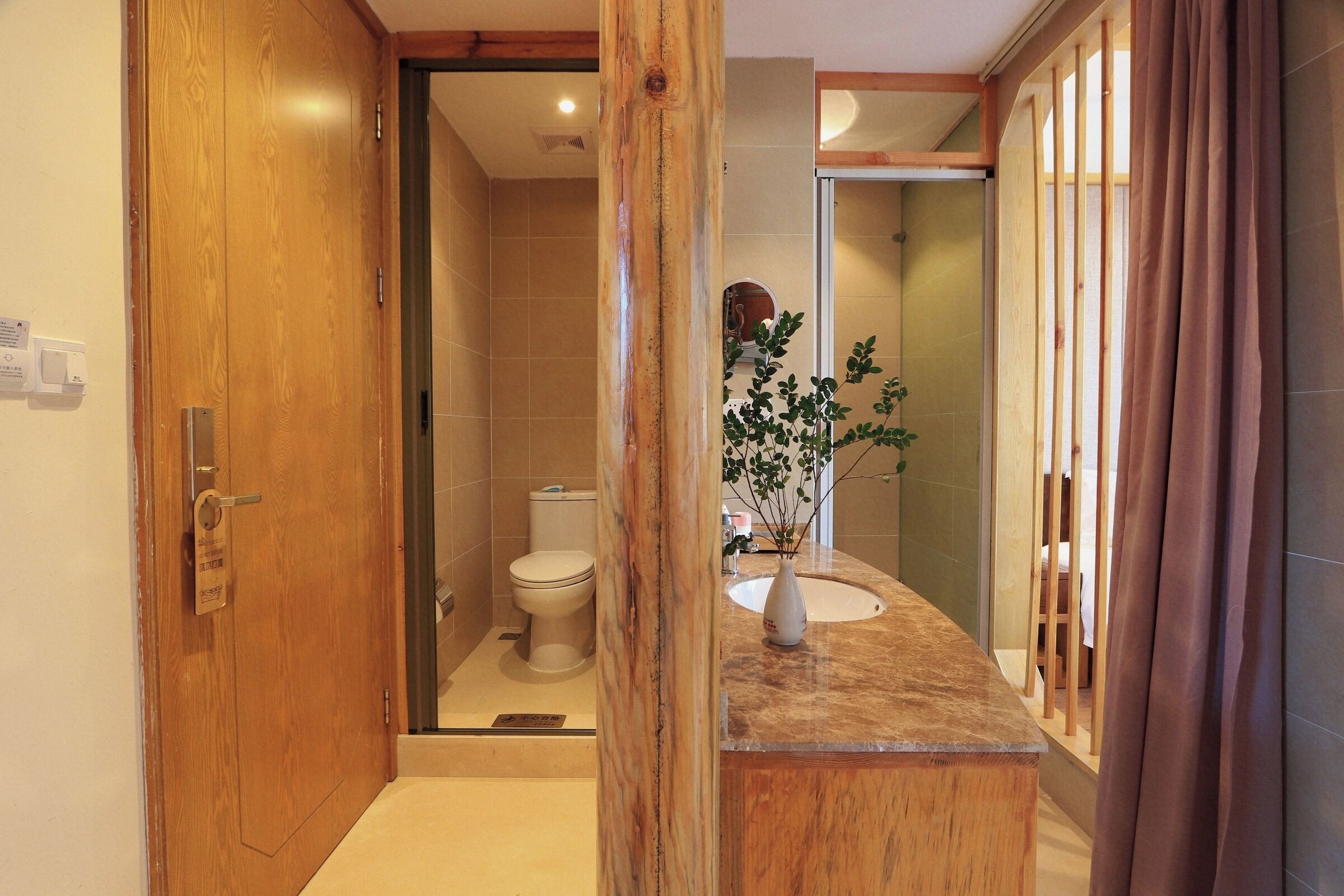 A bathroom with a wooden door, a toilet, a sink with a vase, and a shower area.