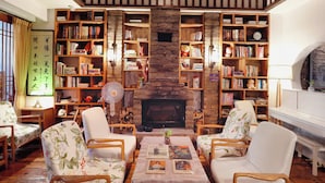 A cozy living room with a fireplace, wooden bookshelves, and floral armchairs. - Mild Spring Boutique Hotel (Huangshan)