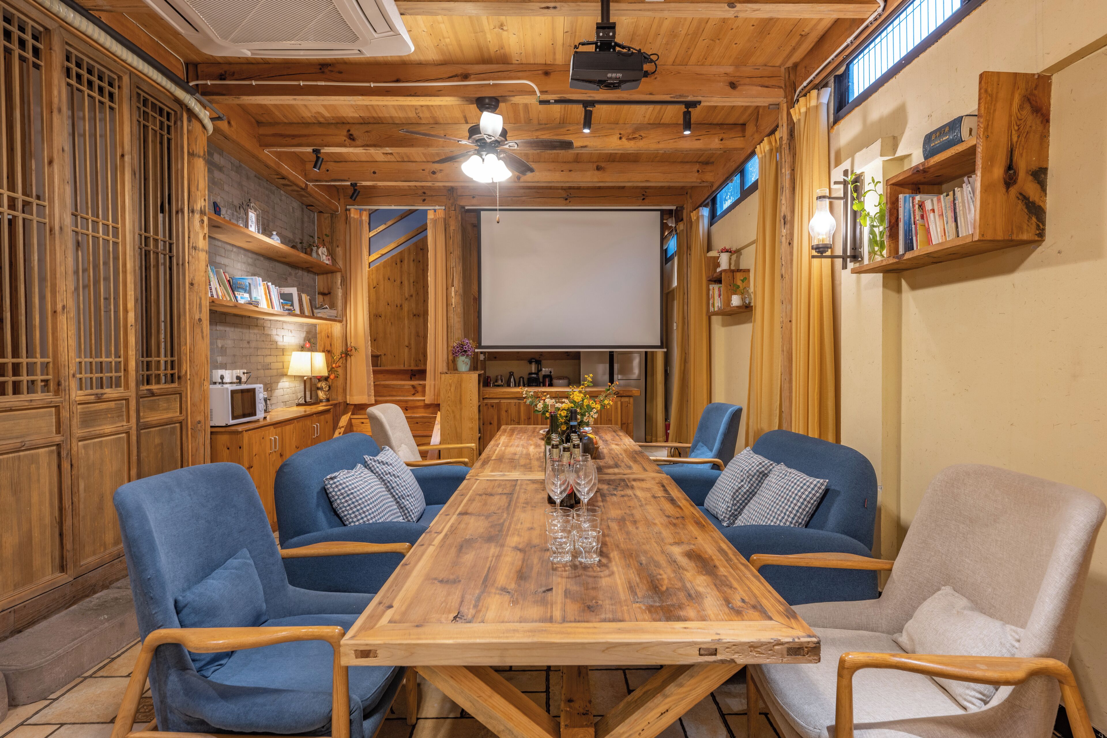 A wooden dining room with a large table, blue upholstered chairs, and a projector screen.