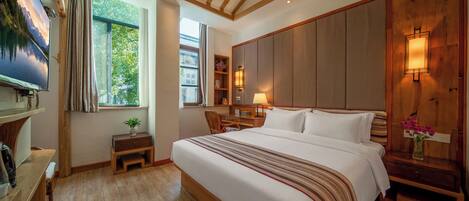 A hotel room with a large bed, a desk, a chair, a nightstand, a lamp, a TV, and a window with curtains.