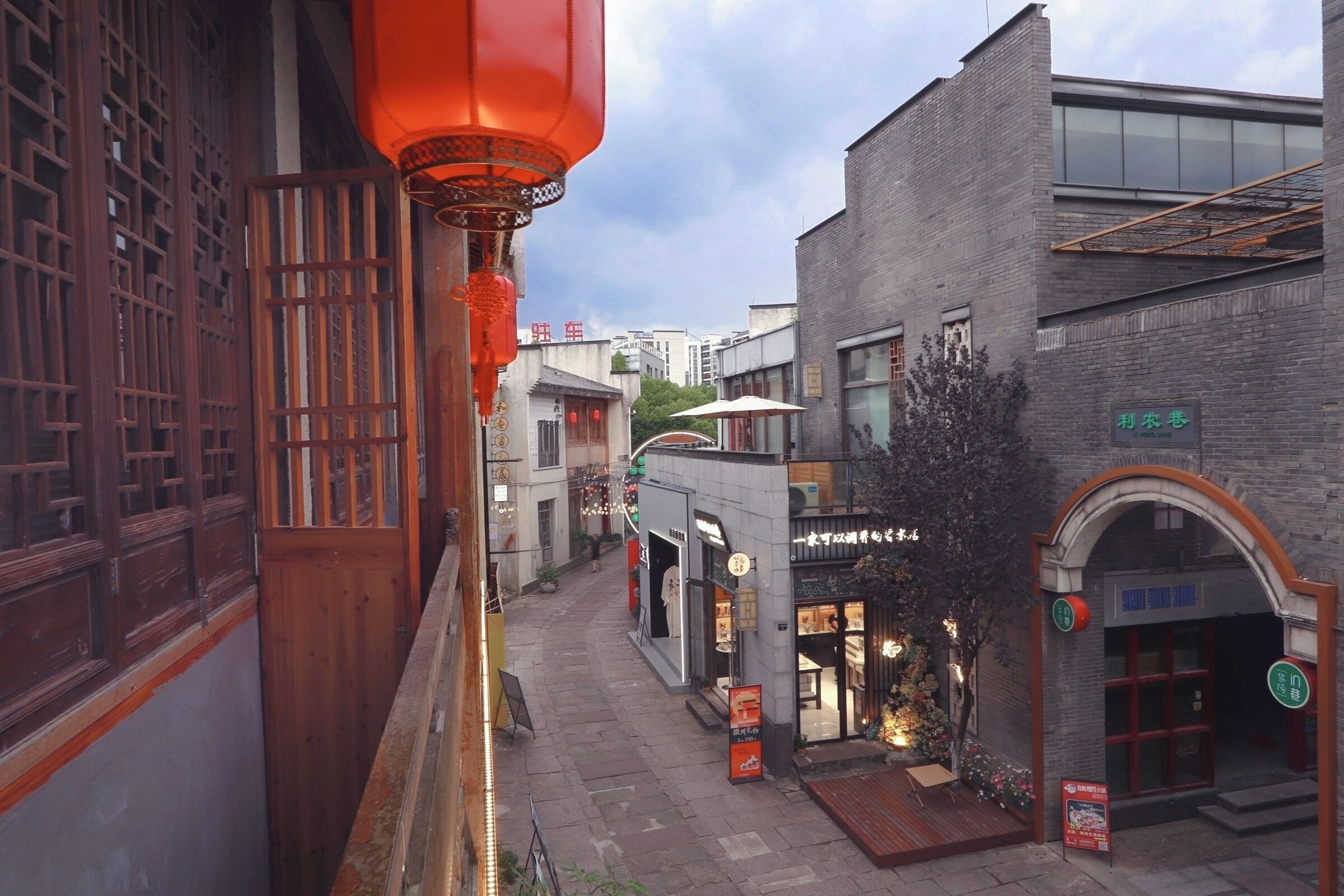A narrow street with traditional wooden buildings, a modern glass building, and a red lantern.