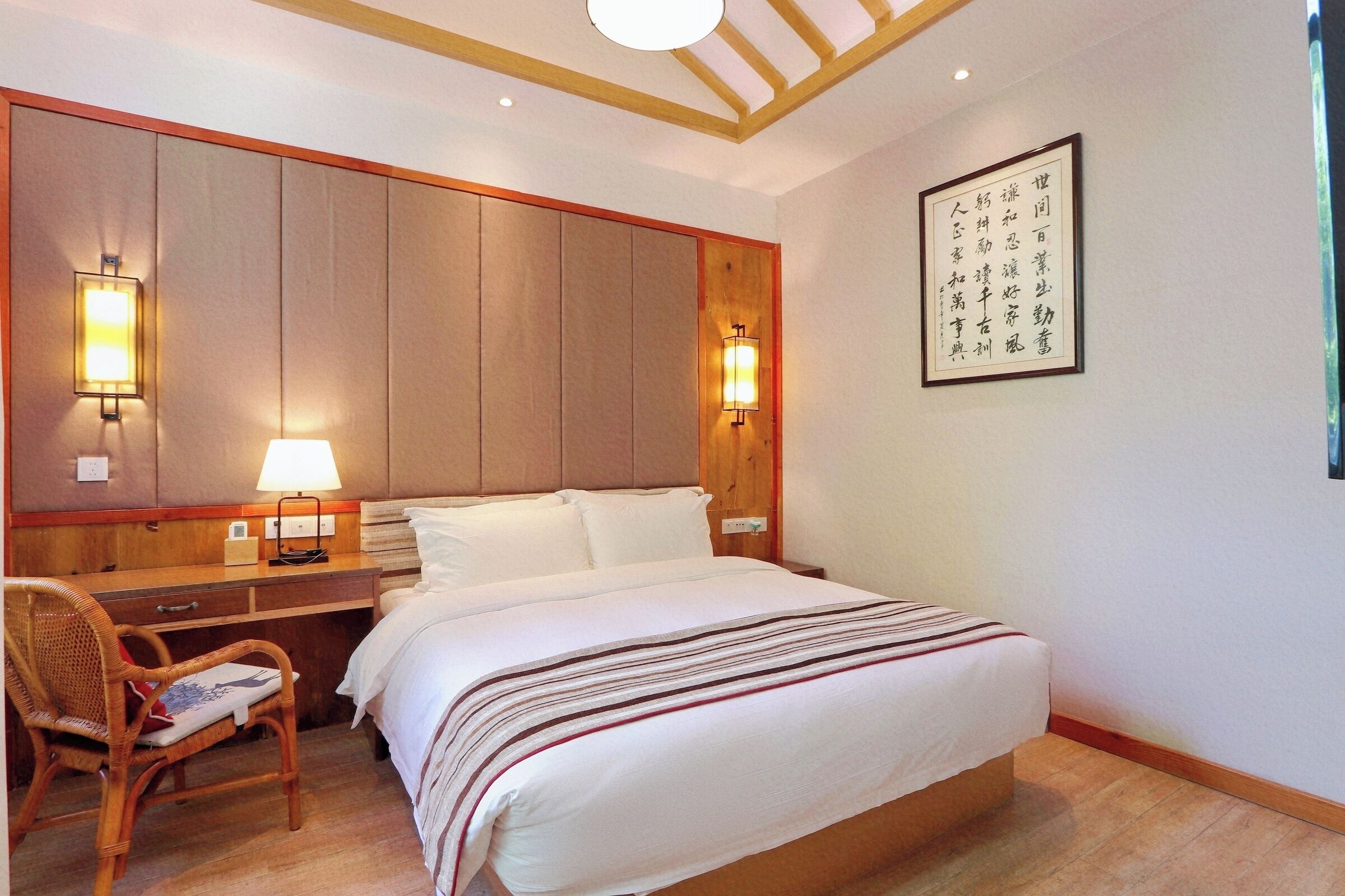 A hotel room with a large bed, bedside lamps, a desk, and a chair.