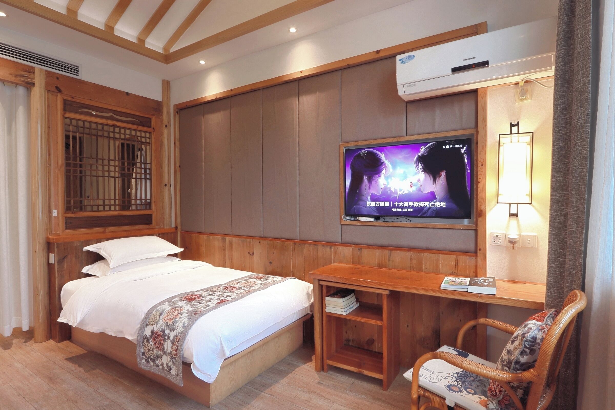 A hotel room with a bed, a TV mounted on the wall, a wooden desk, and a chair.