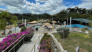 Ein Poolbereich mit mehreren Pools, umgeben von Stufen und Sonnenschirmen, vor der Kulisse von Bäumen und Hügeln.