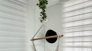 Ein Zimmer mit einem Hängekorbstuhl aus Makramee, weißen Wänden und einem Fenster mit Jalousien.