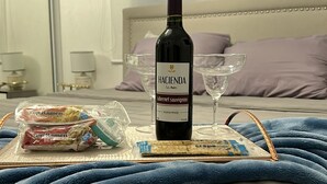 Ein Bett mit einer Weinflasche, Ramen-Nudeln und einem Weinglas auf einem Tablett.