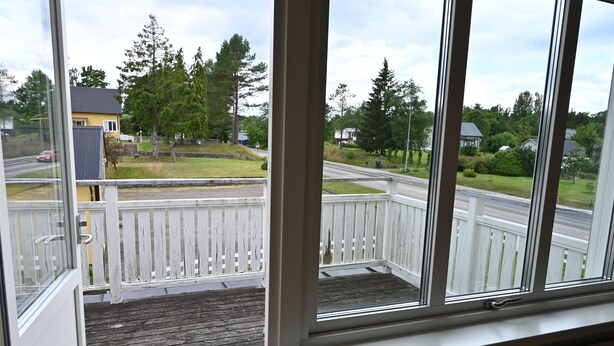 A balcony with a white railing, a view of a road, and houses in the background.