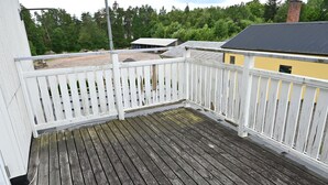 A wooden deck with white railings, surrounded by a white building and a yellow building with a dark roof.