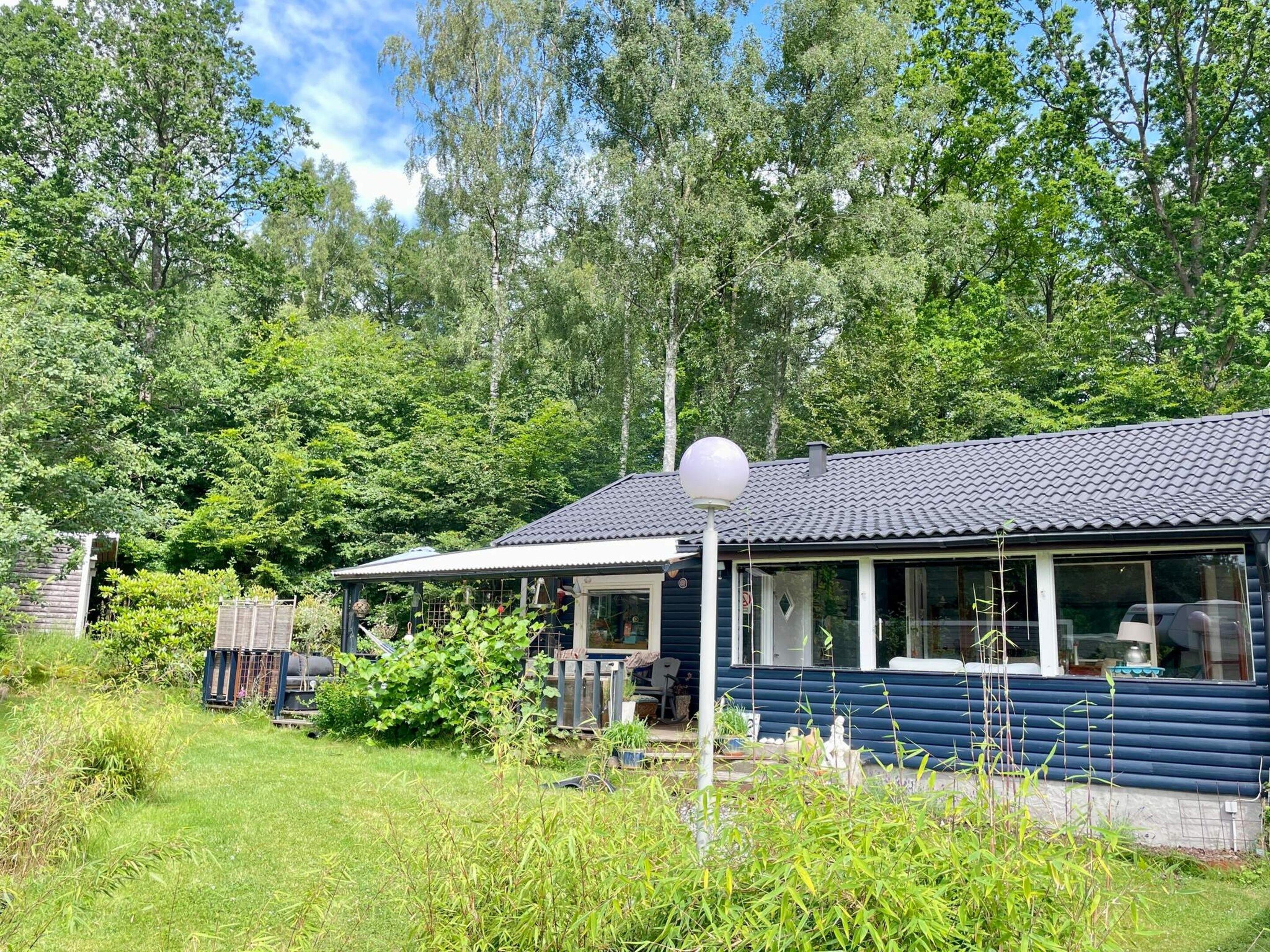 A blue cabin with a tiled roof, surrounded by lush greenery and trees.