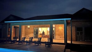 A modern house with a covered outdoor area featuring a pool, outdoor seating, and a well-lit interior.