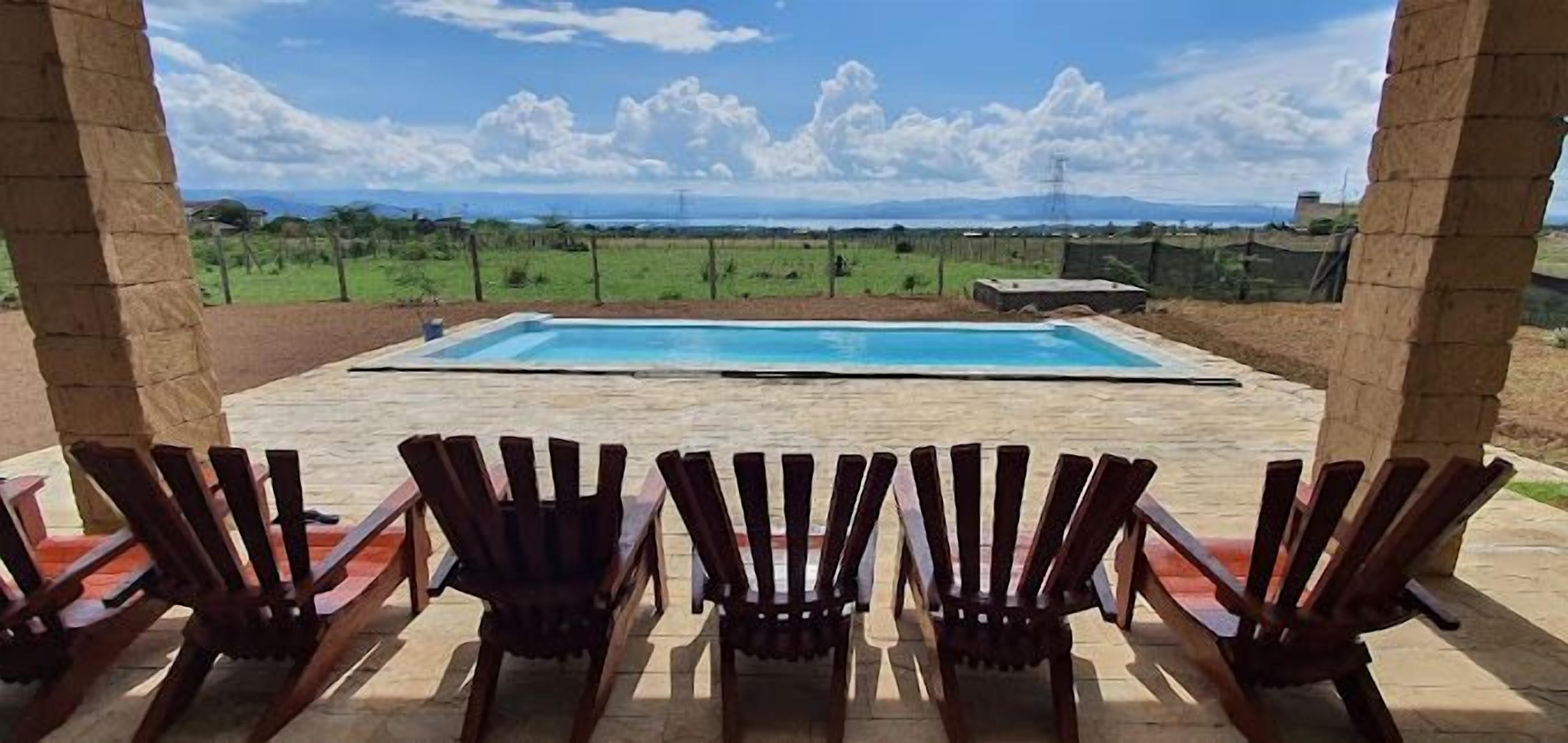 Un espace piscine avec des chaises en bois et une vue sur un paysage verdoyant.