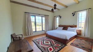 A spacious bedroom with a large bed, wooden beams, and multiple windows.