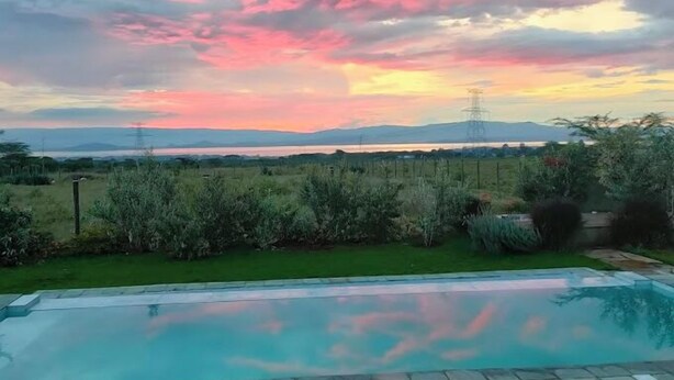 A swimming pool with a view of a sunset over a landscape with mountains and a body of water in the distance.