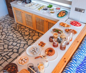 A buffet table with various food items and drinks, a seating area with patterned cushions, and a stone-tiled floor. - Kaşhan Hotel (Kas)