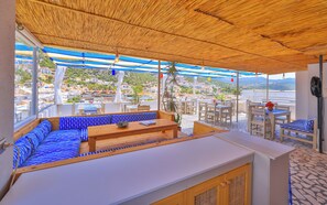 A terrace with a wooden ceiling, white furniture, and a view of a coastal town. - Kaşhan Hotel (Kas)