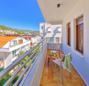A balcony with a table, chairs, and a view of buildings and hills. - Kaşhan Hotel (Kas)