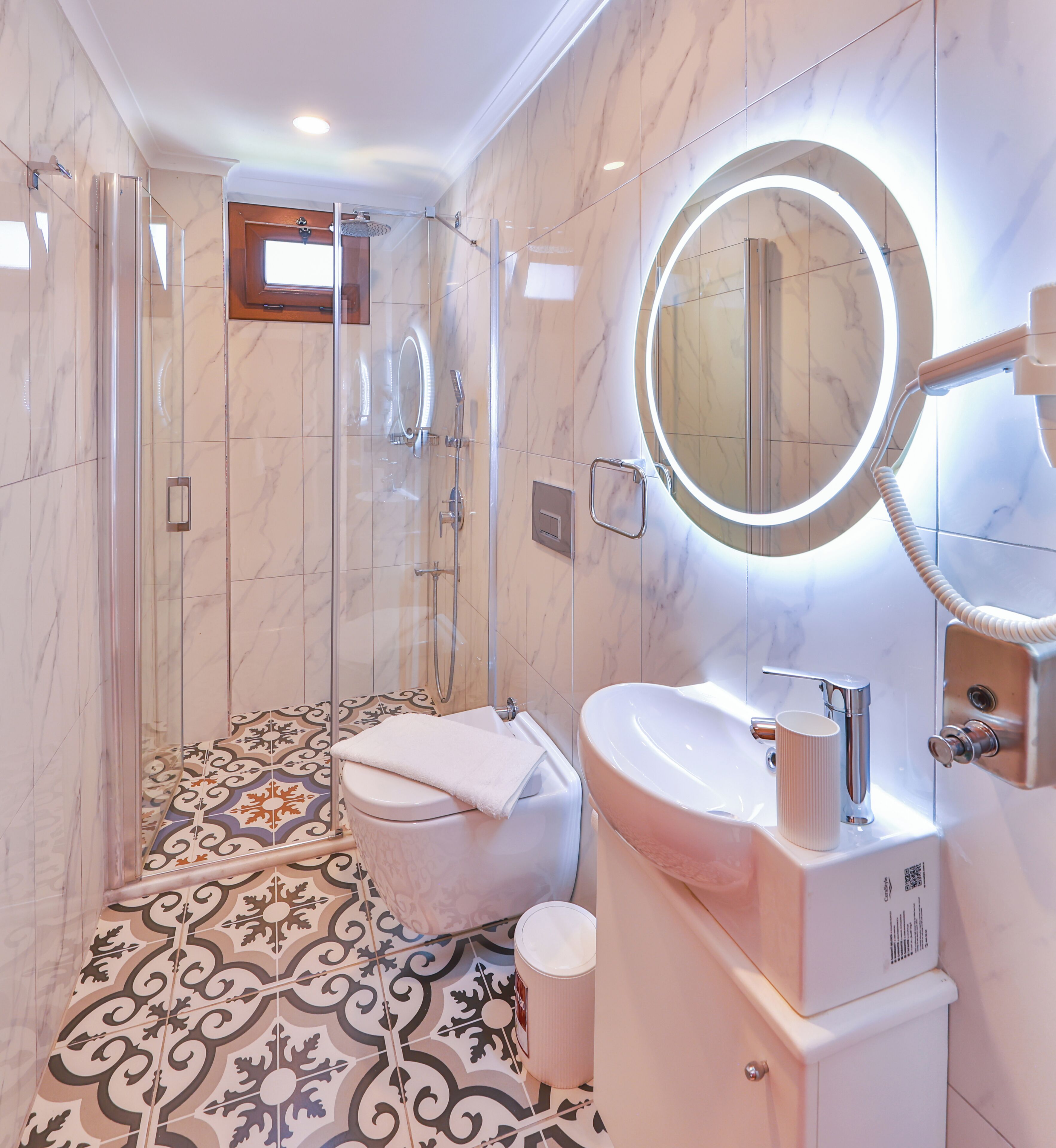 A bathroom with a glass-enclosed shower, a sink with a mirror, and patterned floor tiles.