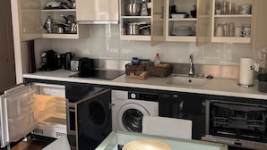 A modern kitchen with built-in appliances, a dining area with a glass table, and a laundry machine. - Chic 1-bedroom apartment with WiFi, AC in fabulous london Muslim douche 4 people (London)