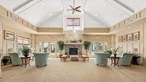 Un salon spacieux avec un haut plafond, une cheminée et deux fauteuils verts.