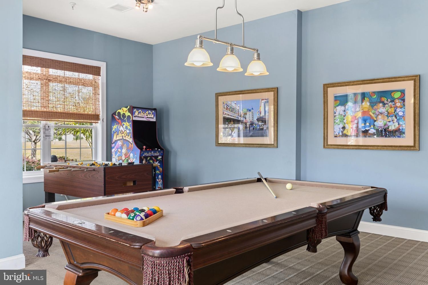 A pool table in a room with blue walls, a framed picture, and a Multi-Cade arcade machine.