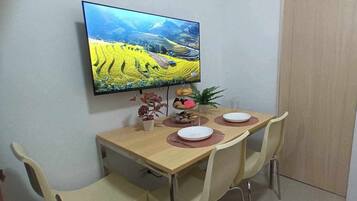 A dining area with a table set for two, a television mounted on the wall, and a door to the right.