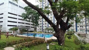 A residential building with a swimming pool, surrounded by greenery and a large tree.