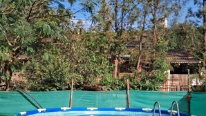 A blue above-ground pool with a ladder, surrounded by greenery and trees. - Laxmi villa (Varanasi)