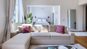 Ein modernes Wohnzimmer mit einem beigefarbenen Ecksofa, einem Couchtisch und einem großen Fenster mit Vorhängen.