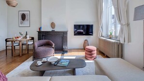 Ein Wohnzimmer mit Kamin, Fernseher, Esstisch mit Stühlen und einer Couch.