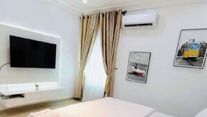 Une chambre d’hôtel équipée d’un lit, d’un téléviseur à écran plat fixé au mur, d’un appareil de climatisation et de deux tableaux encadrés accrochés au mur.