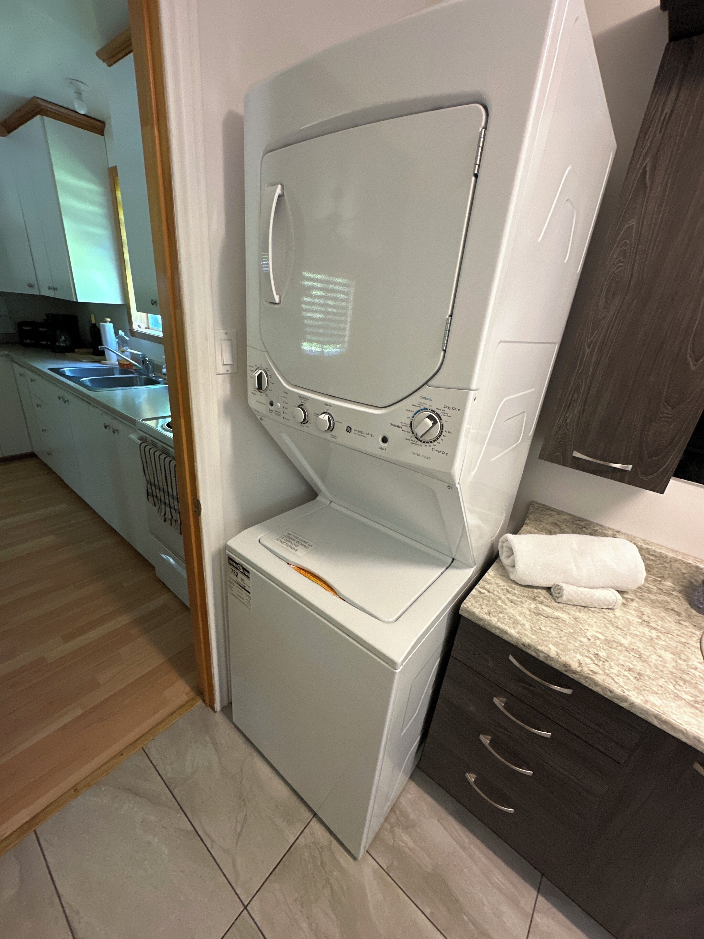 A compact washer and dryer unit in a modern kitchen with a wooden floor and dark cabinetry.