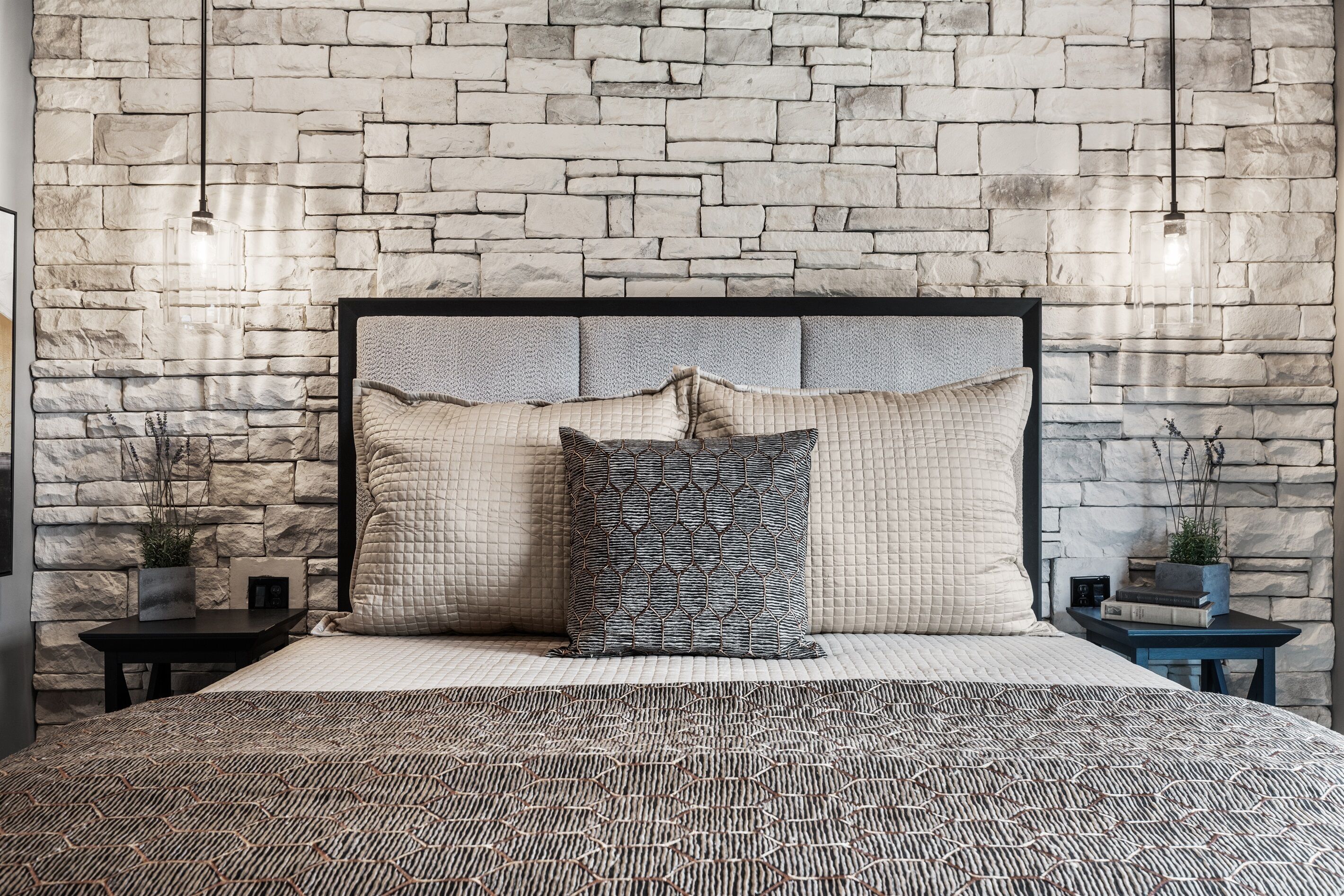 A bedroom with a stone wall, a bed with patterned bedding, and two nightstands with decorative items.