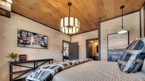 Ein modernes Schlafzimmer mit Holzboden, einem großen Bett mit gestreiftem Kopfkissen, einem Nachttisch mit Buch und Pflanze sowie einem Stadtbild an der Wand.