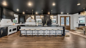 Een moderne keuken met een centraal eiland, barkrukken en een groot fornuis.