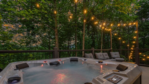 A hot tub surrounded by a deck with string lights, overlooking a forested area. - New!Min Away from Gatinburg,Pool Table, (Gatlinburg)