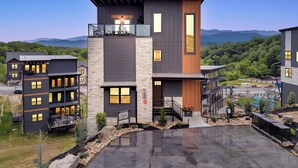 A modern multi-story building with a balcony, a stone facade, and a view of mountains. - Smoky Mtn Luxury Cabin, FREE Waterpark, PS5, Pool Table, Indoor Pool, Mini Golf (Sevierville)