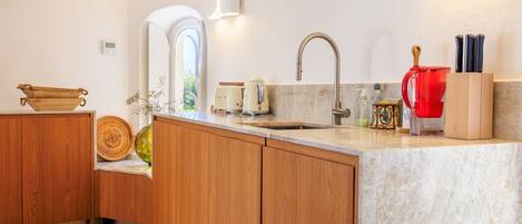 A modern kitchen with wooden cabinets, a marble countertop, a sink, and a red kettle.