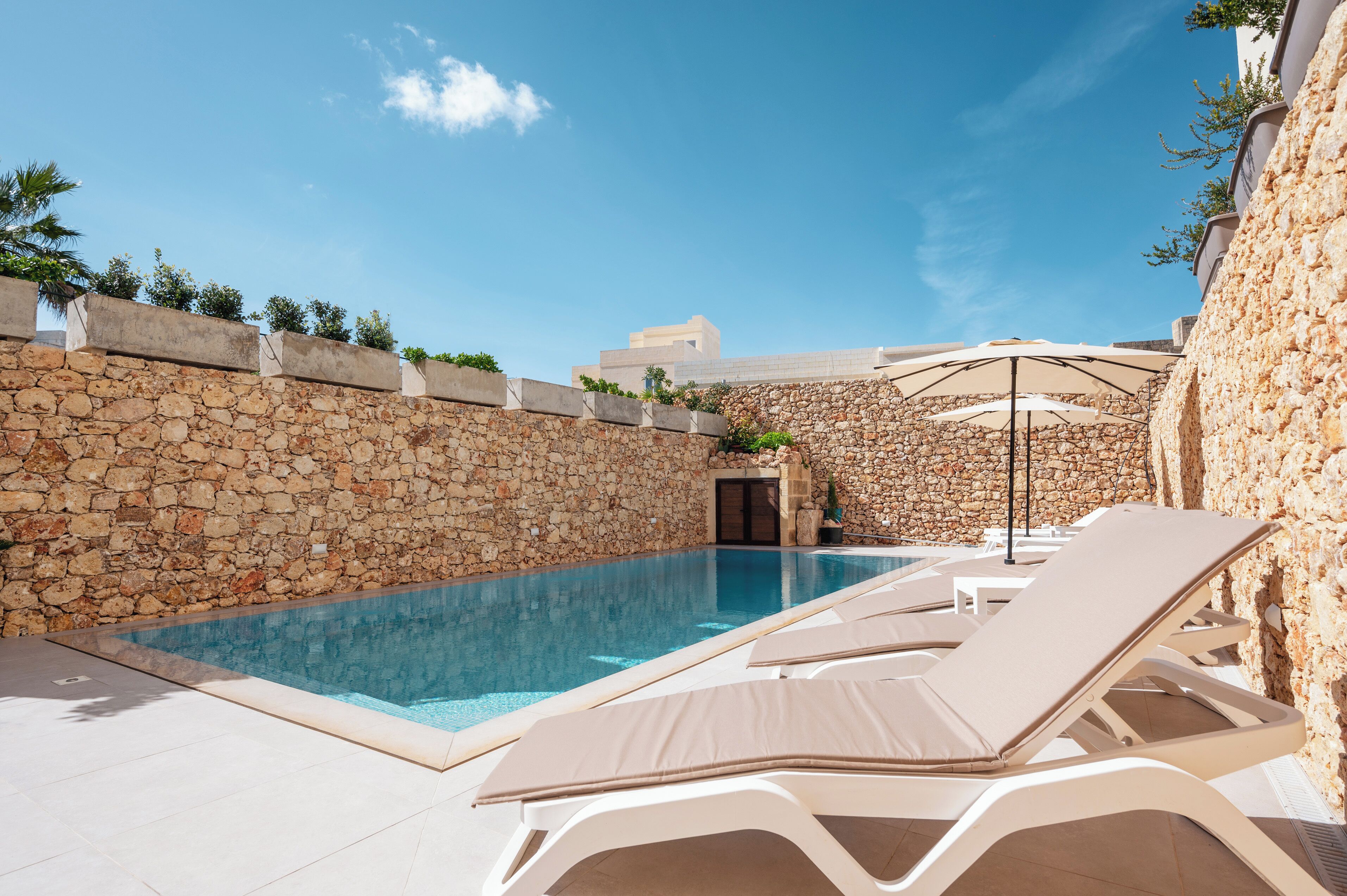 A swimming pool with lounge chairs, stone walls, and a clear sky.