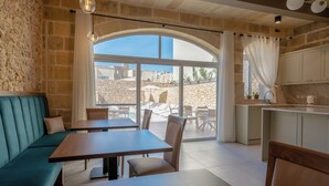 A modern interior with a stone wall, a seating area with a sofa and tables, a kitchen area, and a view through large windows. - Silla Boutique B&B (Xagħra)