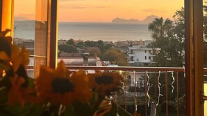 Un balcon offrant une vue sur la mer et les montagnes lointaines au coucher du soleil.