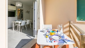 An open balcony with a dining table set for two, a small table with a pitcher and glasses, and a view into the adjacent room with a dining table and chairs. - Nice apartment for 5 guests with A/C, WIFI, TV, patio and pets allowed (Cecina)