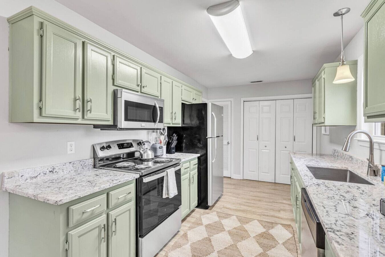 Una cocina con gabinetes verdes, un refrigerador de acero inoxidable, un microondas, una estufa y un lavamanos.