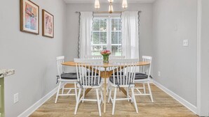 A dining area with a round table, white chairs, and a chandelier.
