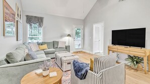 A spacious living room with a grey sofa, striped armchair, and a television on a wooden stand.