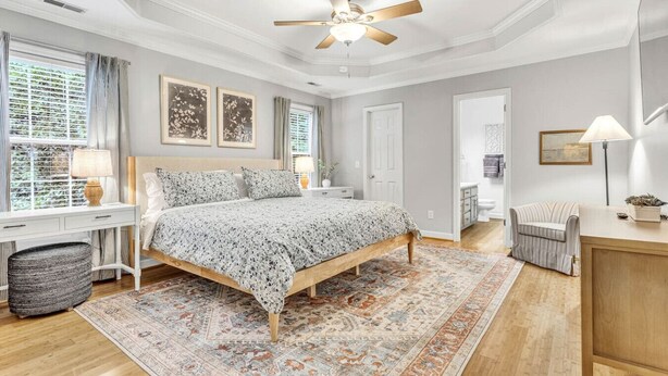 A bedroom with a bed, bedside tables, a ceiling fan, a window with curtains, a rug, and a chair.